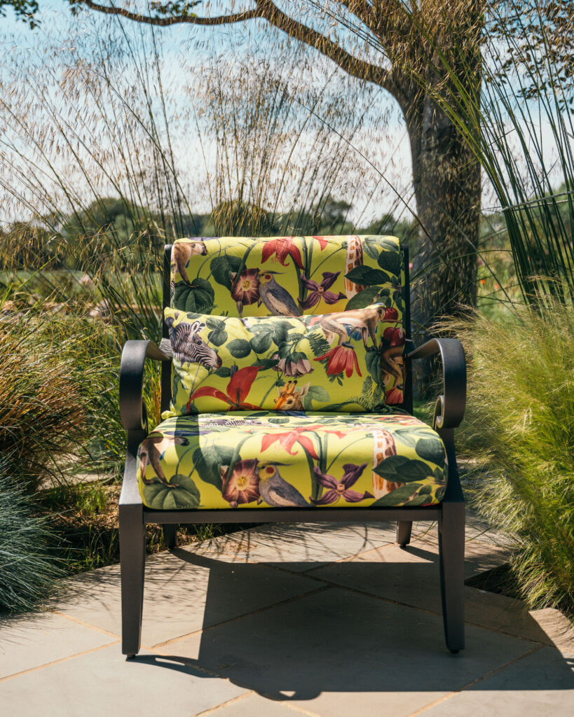 Luxury outdoor armchair with vibrant botanical and bird-themed upholstery, set in a lush garden setting, showcasing 2025 sustainable outdoor furniture trends.