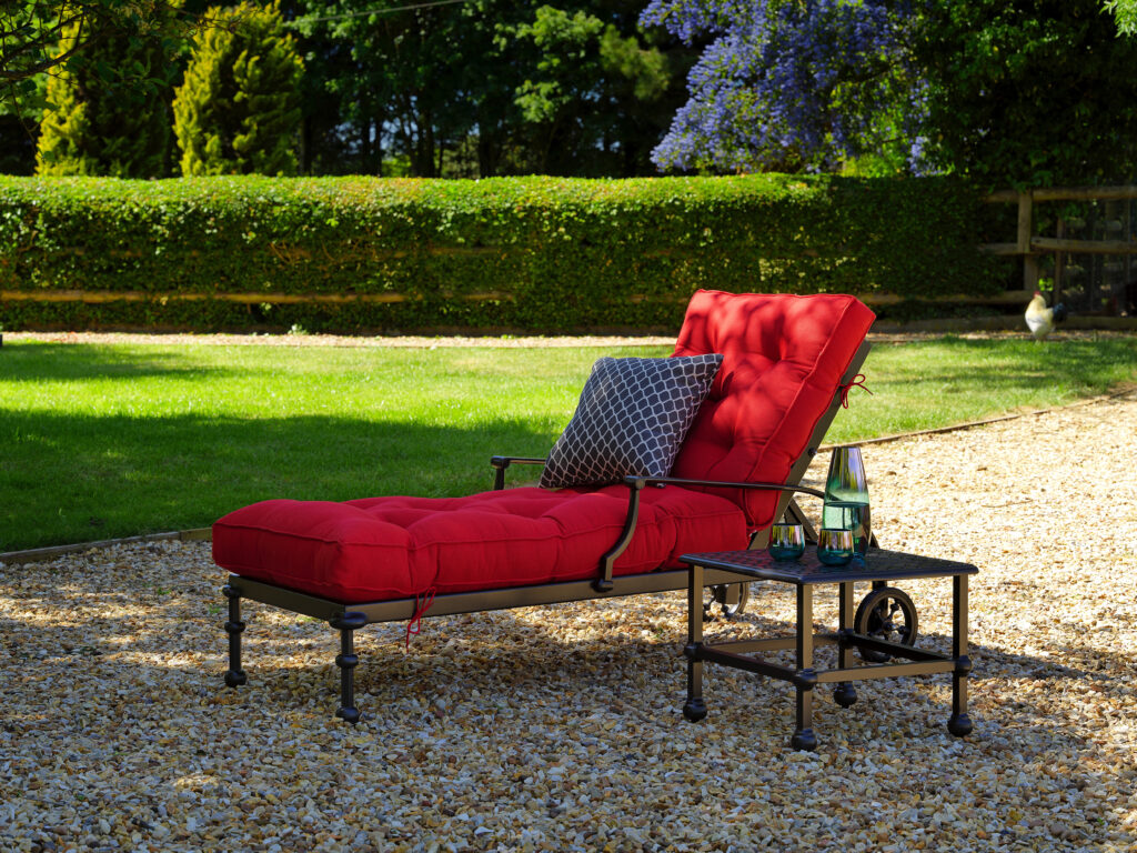 Luxurious outdoor chaise lounge with plush red cushions and a stylish side table, designed for ultimate comfort and ergonomic relaxation in garden spaces.
